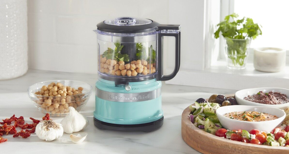 A teal KitchenAid® food chopper next to a platter of crudités